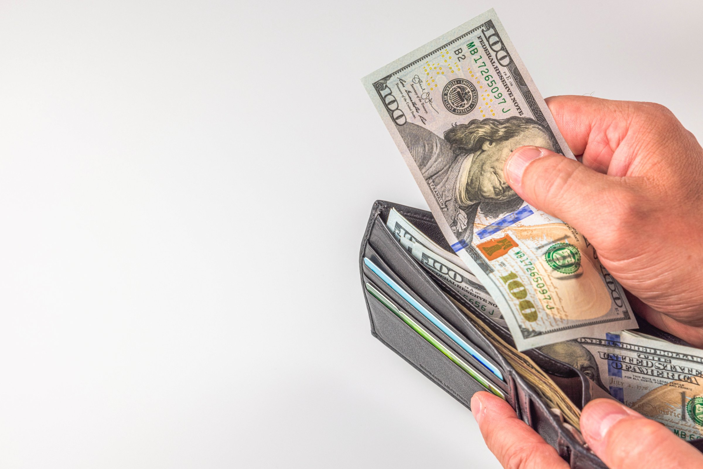Sweden. Uppsala. 03.18.2024. Close-up view of a person's hand retrieving dollar bills from a wallet.