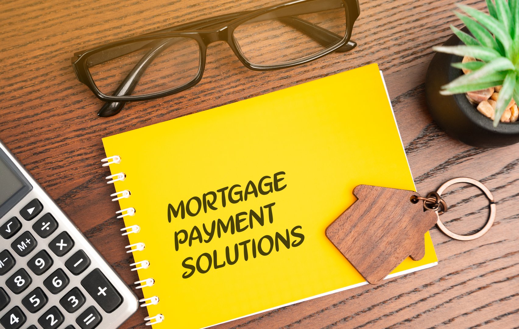 Mortgage payment solutions inscription in notebook. Real estate and finance concept, investment in loan and housing. Glasses, calculator and house keychain