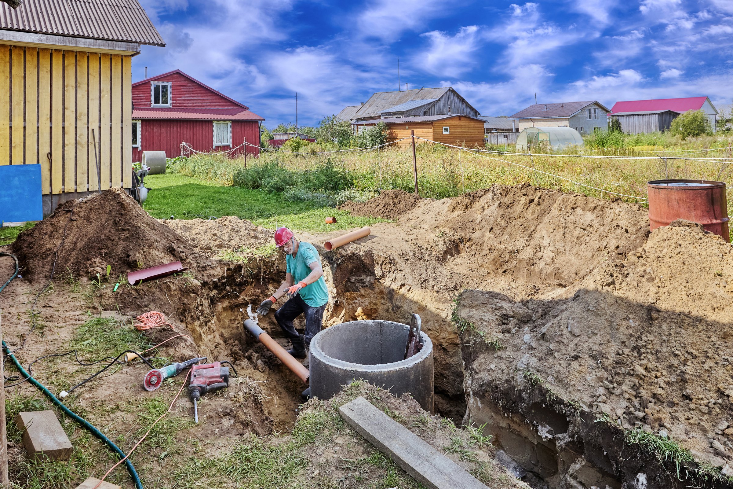 Connecting inlet sewer pipe to concrete ring during installation of septic tank, construction worker takes measurements.