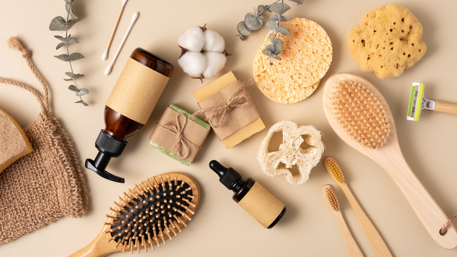 Flat lay of eco-friendly body care, bath and beauty products including bamboo hair and back brushes, soap, and glass bottles.