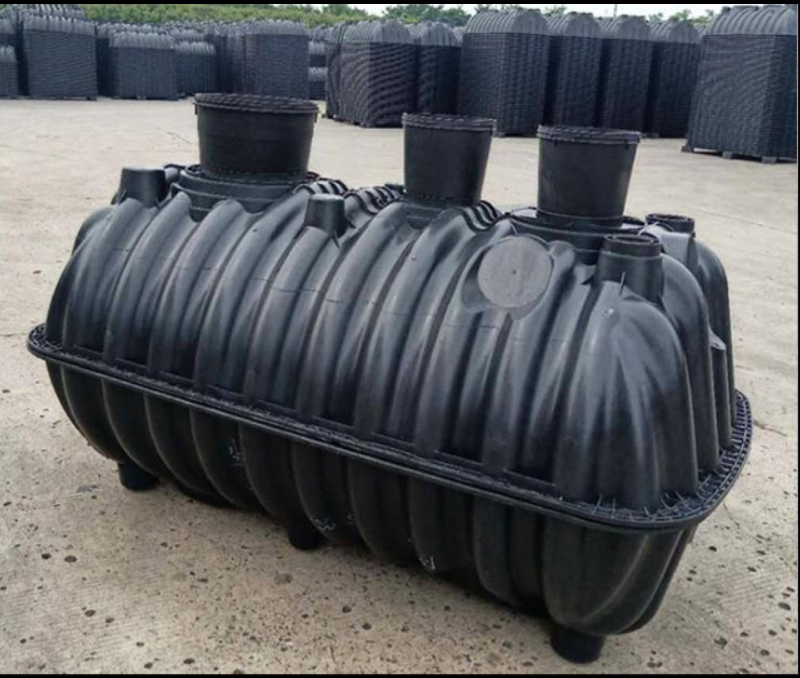 A large black plastic septic tank with multiple openings sits in an outdoor storage area on a concrete surface.
