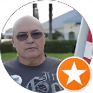 Man wearing sunglasses in front of building, star icon on image corner.