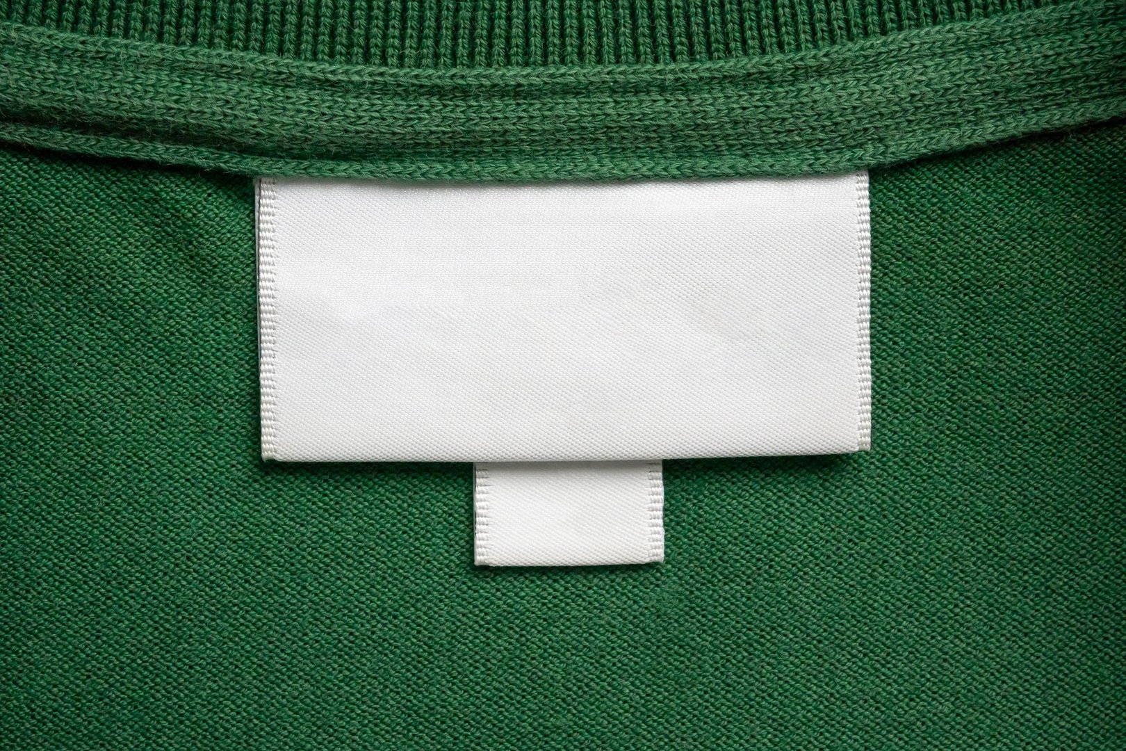 Blank white laundry care clothes label on green shirt fabric texture background