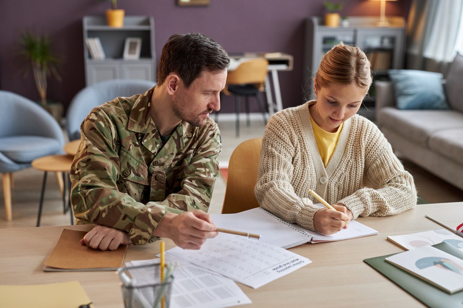 Front view portrait of father wearing military uniform helping daughter with homework