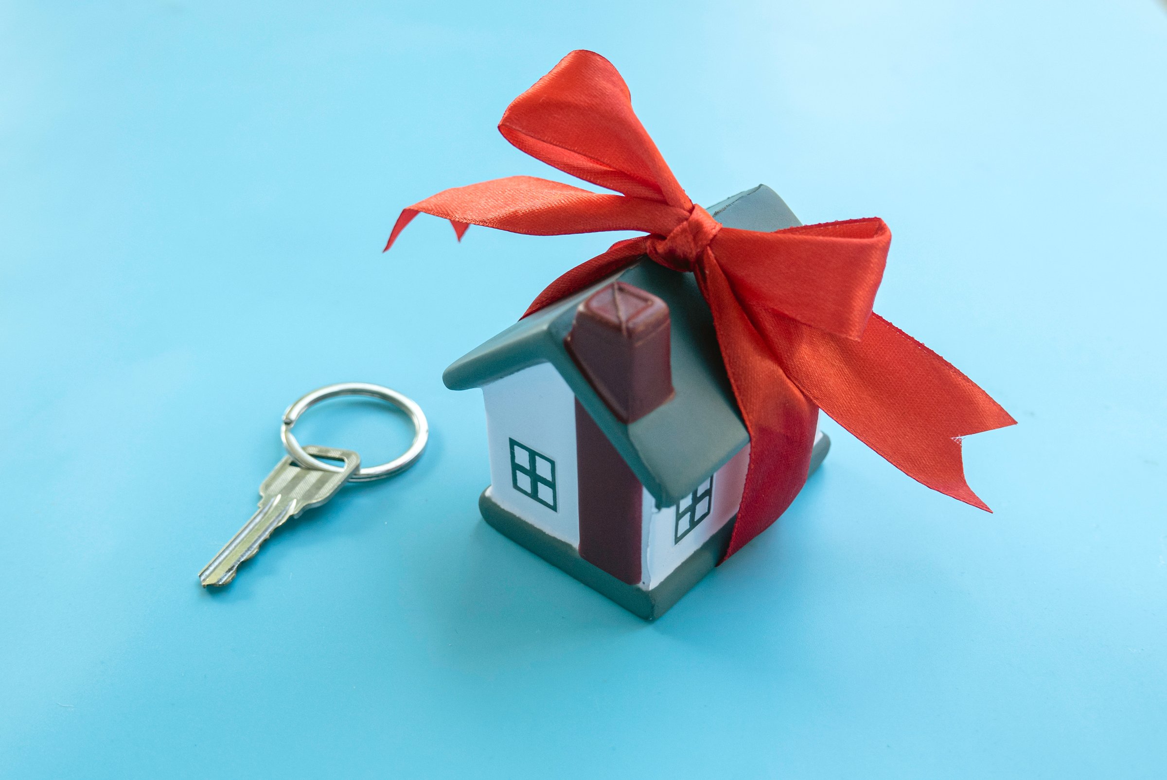 House Key with Miniature House Gift Wrapped with Red Ribbon on blue Surface