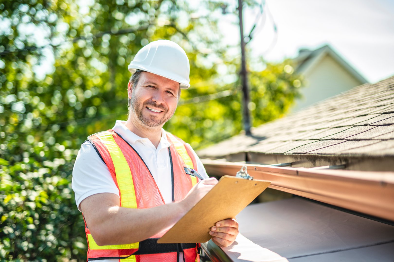 A man with hard hat standing on steps inspecting house roof