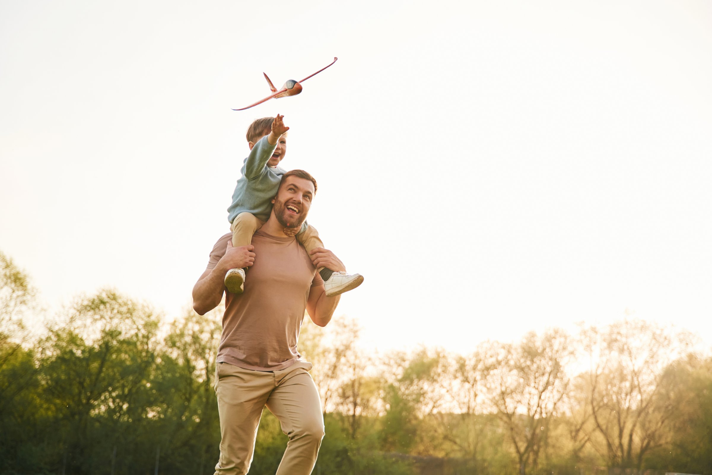 Toy plane is in the air. Happy father with son are having fun on the field at summertime.