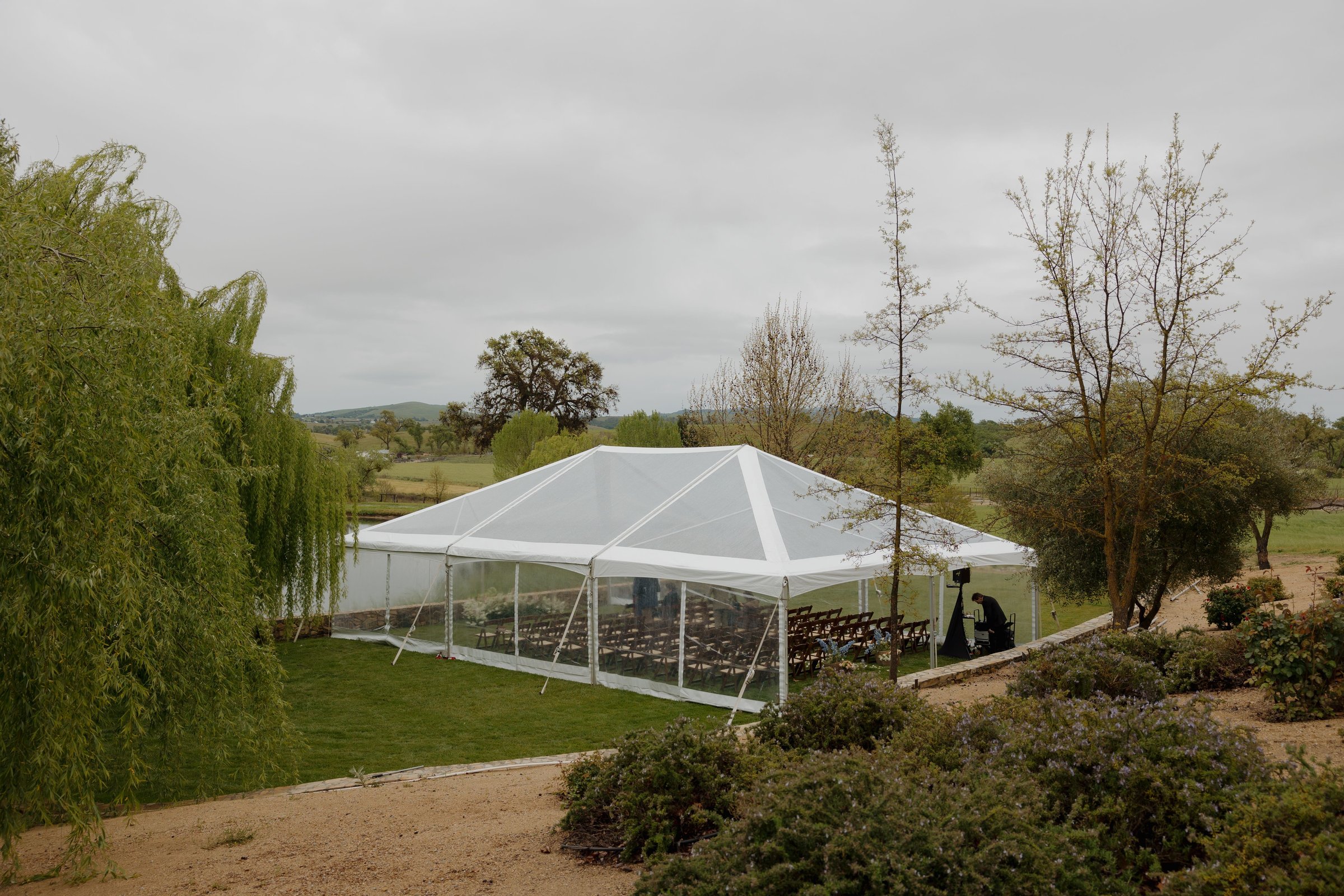 Outdoor event tent set in a scenic landscape with trees and greenery under an overcast sky.