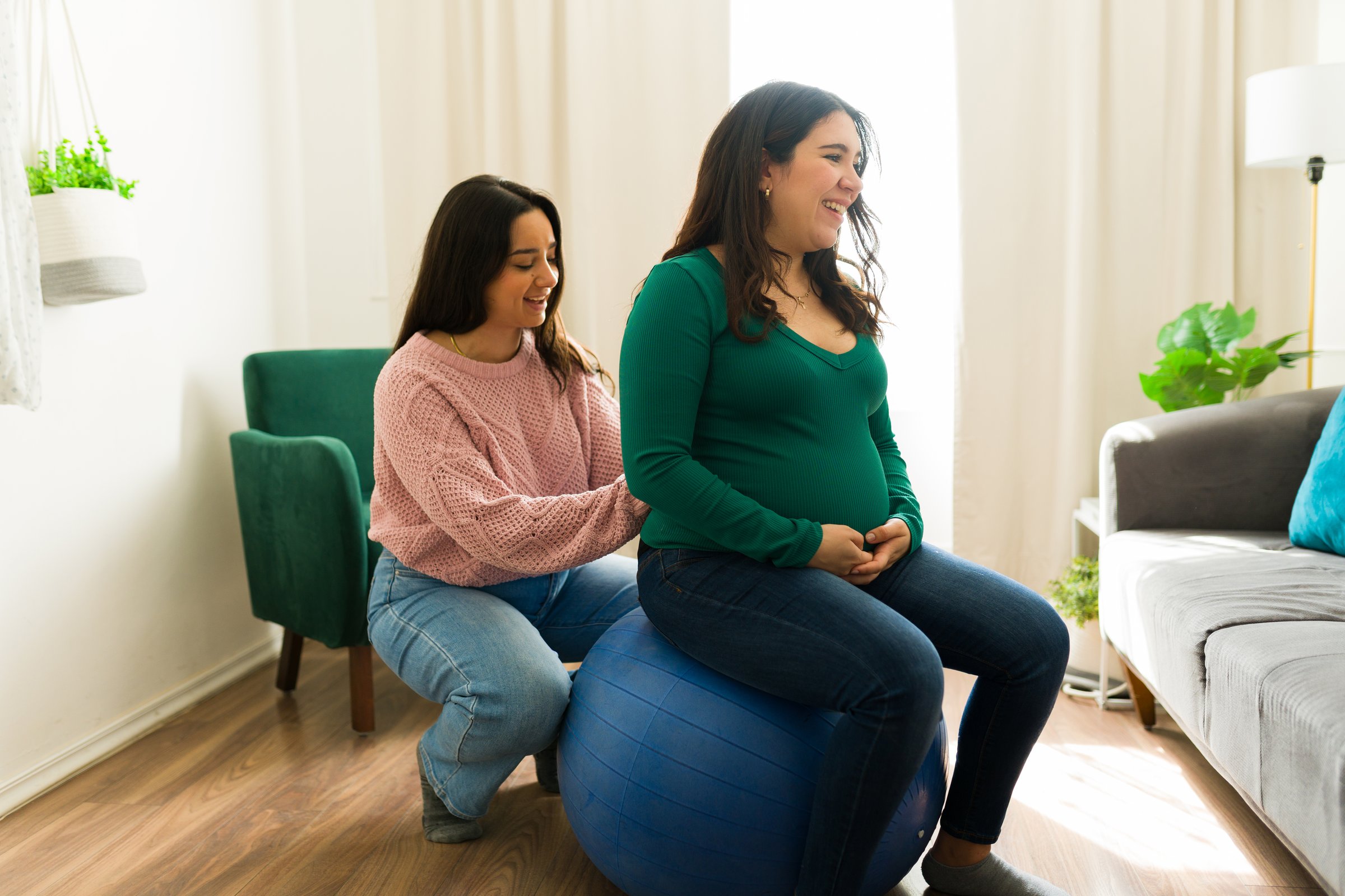 Pregnant woman relaxing on fitness ball, receiving comforting massage from supportive doula during prenatal wellness session