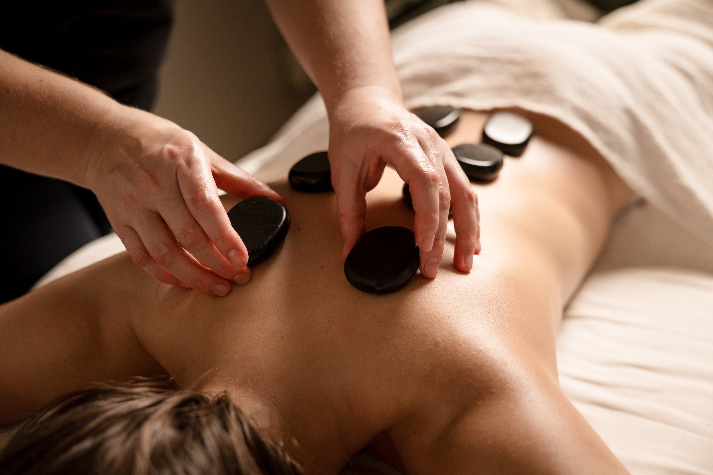 A massage therapist places hot stones on a client's back during a stone therapy session. Hot stone massage concept