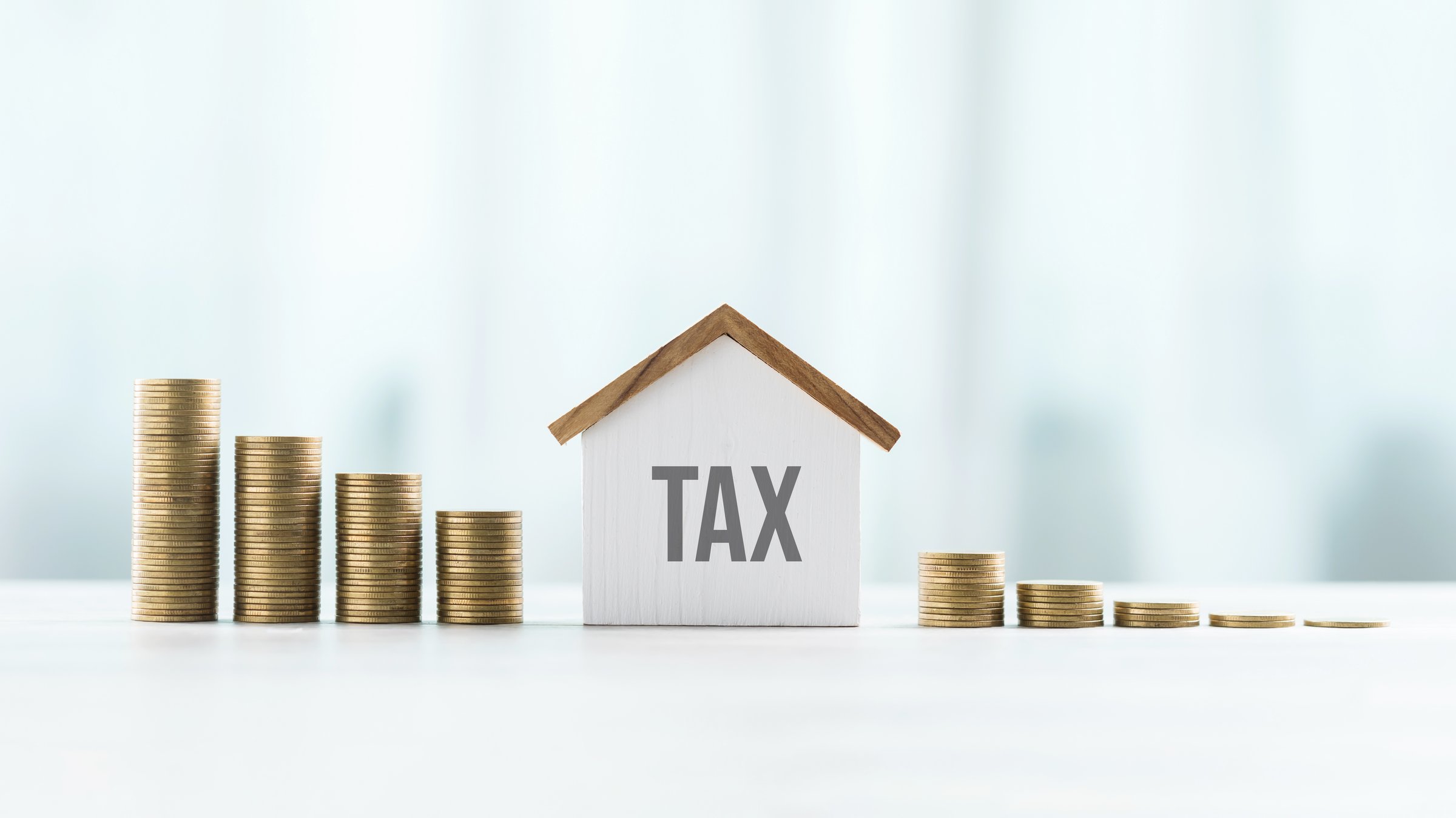 House model and stack of coins on a table against a bright white background, symbolizing the concept of real estate taxes, financial planning, and property investment