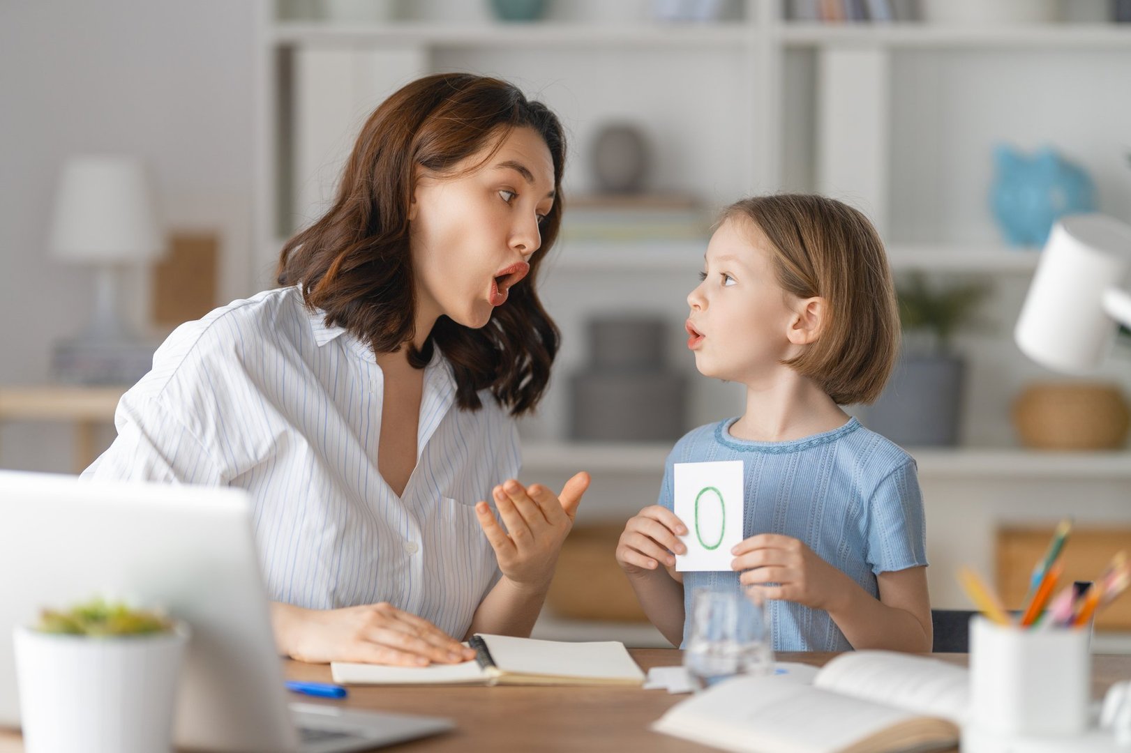 Happy child and adult are sitting at desk. Girl doing homework or online education.