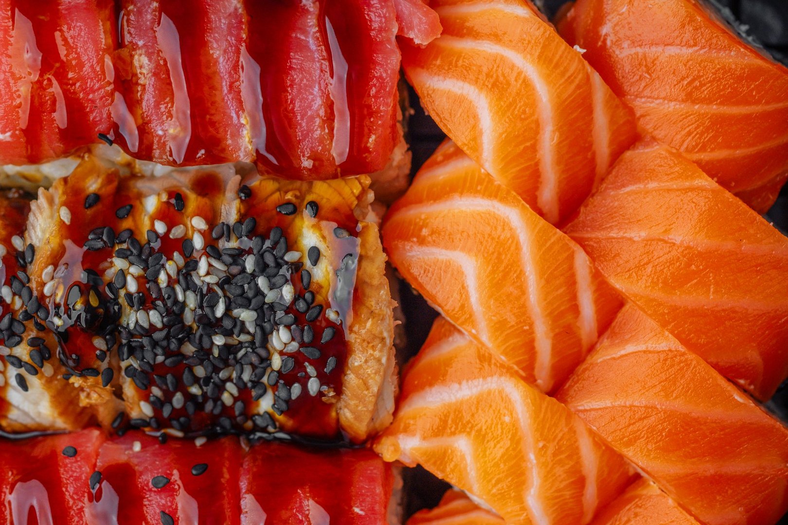 close up assortment of sushi rolls with salmon tuna and eel topped with sesame seeds and sauce