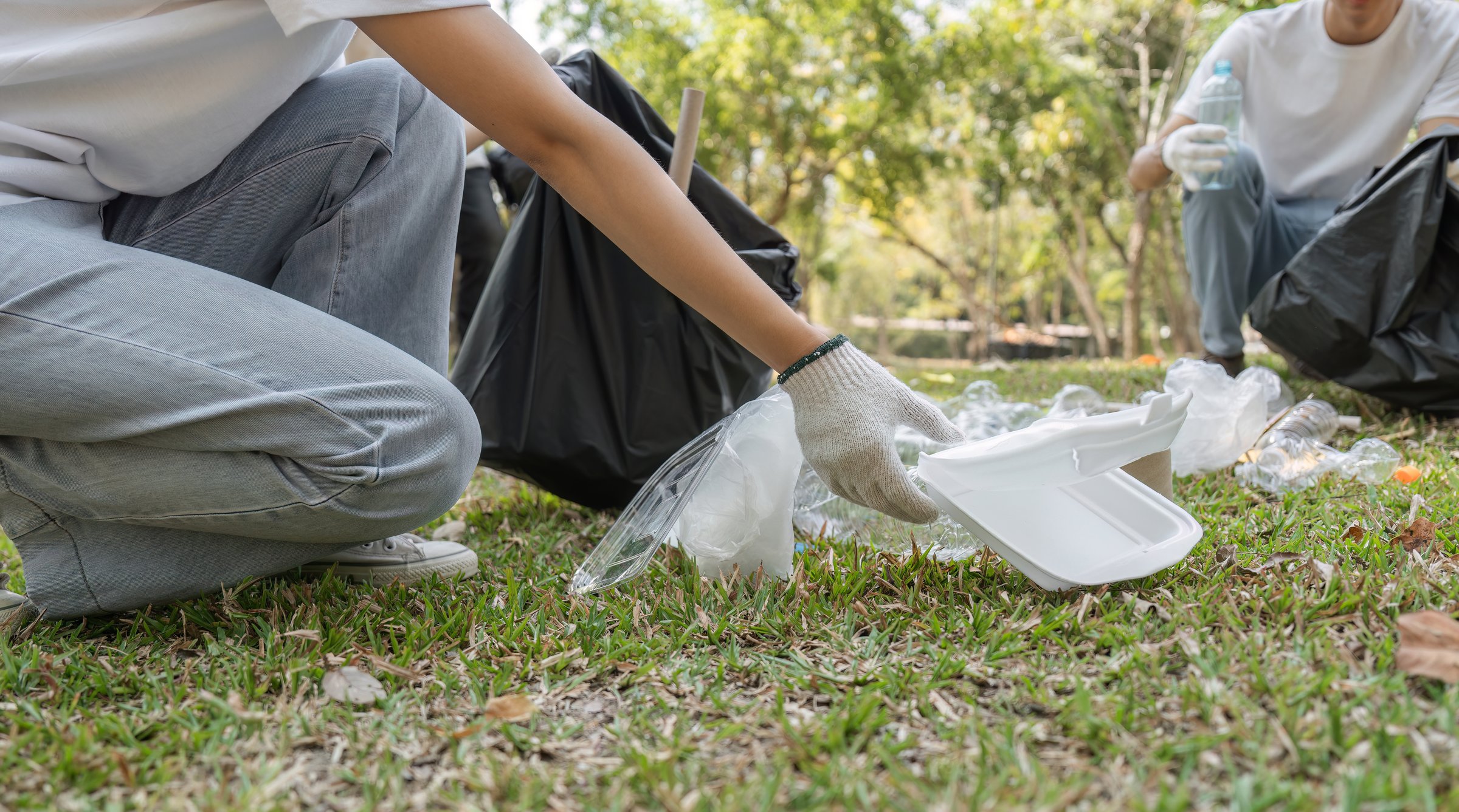 A volunteer is seen picking up trash in a park, promoting a cleaner environment and sustainability.