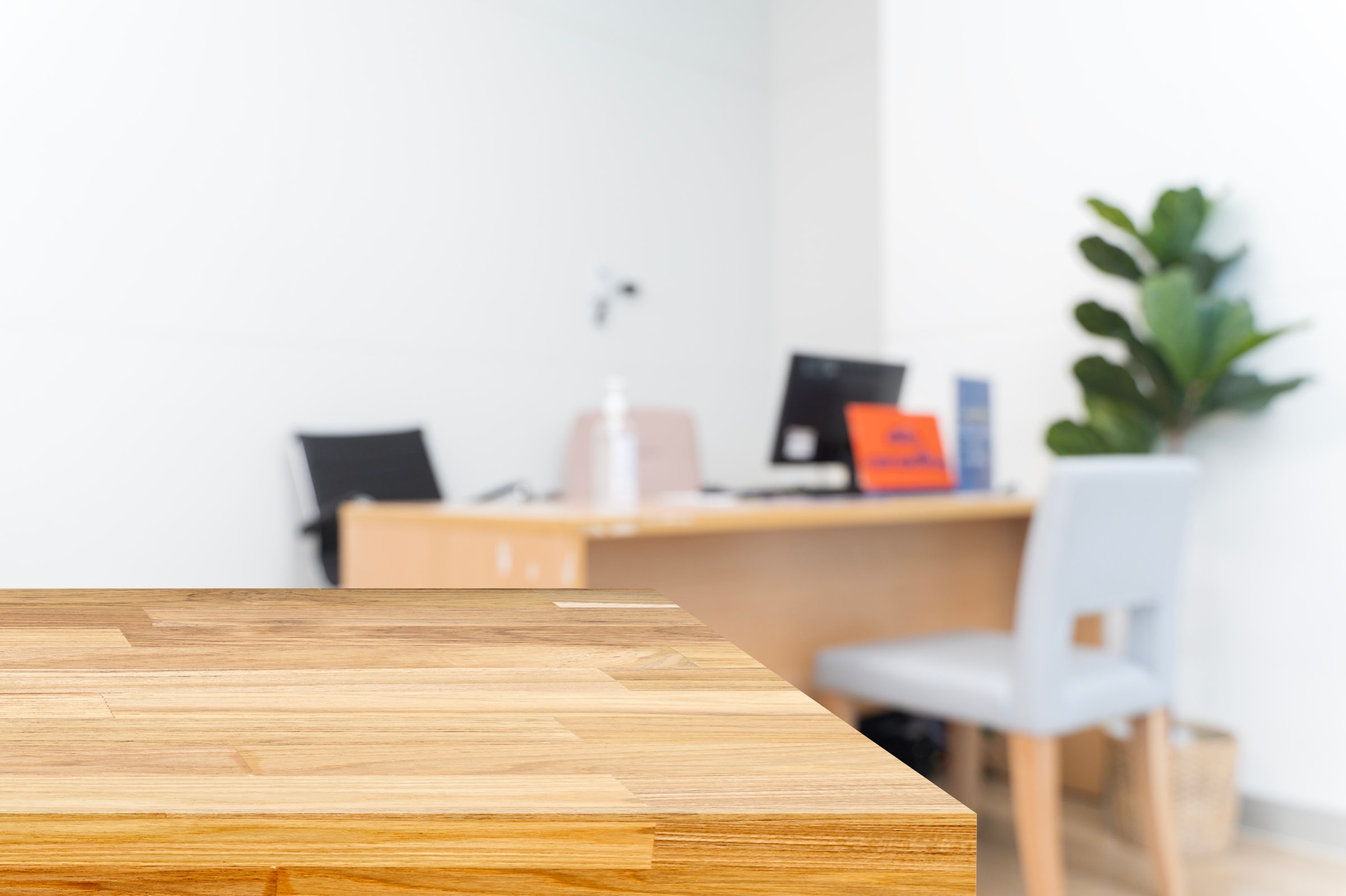 Blurred background of a clean office with modern desk, chair, and computer, featuring an empty wooden table in foreground. Ideal workspace concept with warm and professional atmosphere.