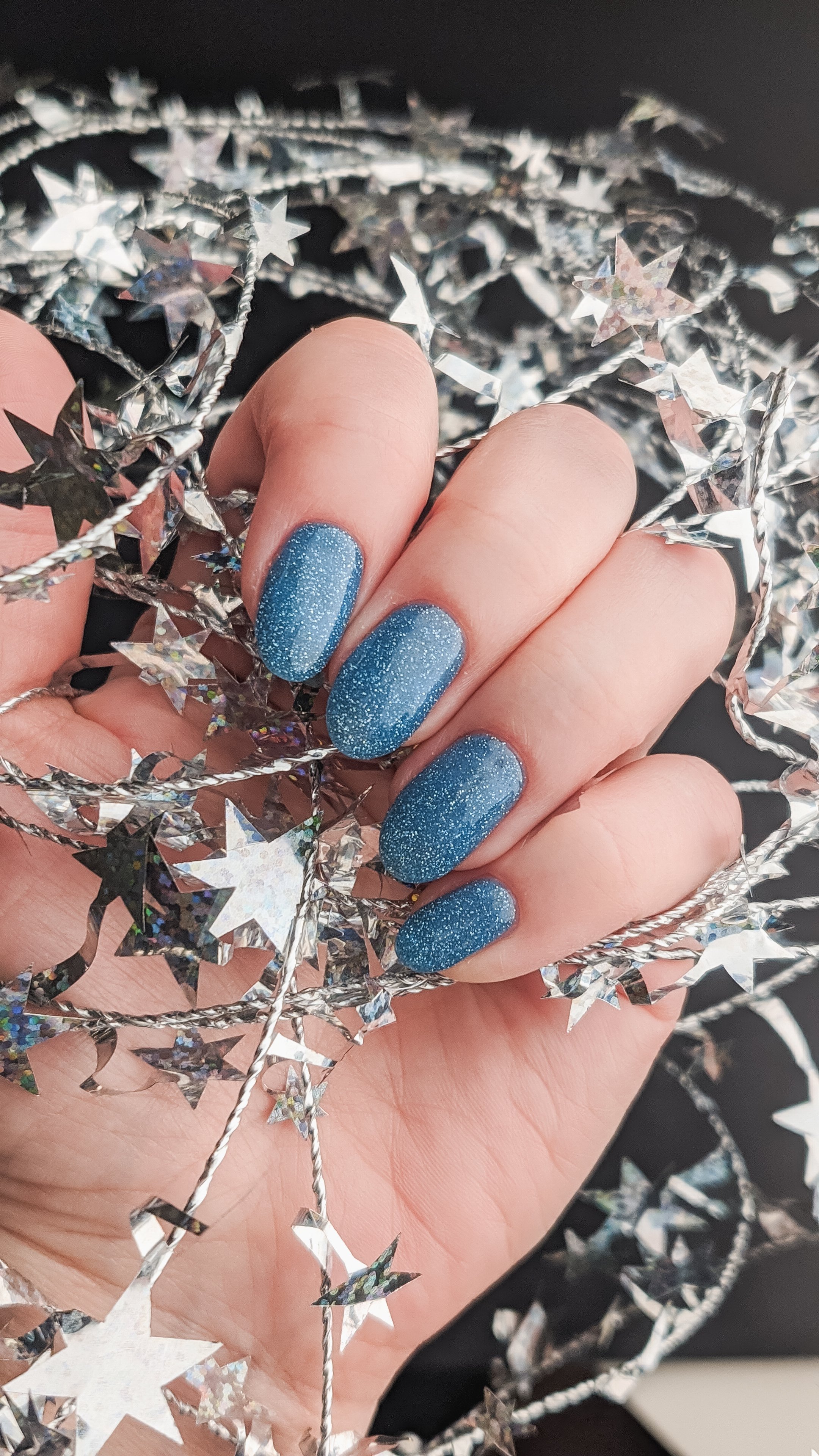 Blue glitter nail art displayed with silver star decoration, close-up view.