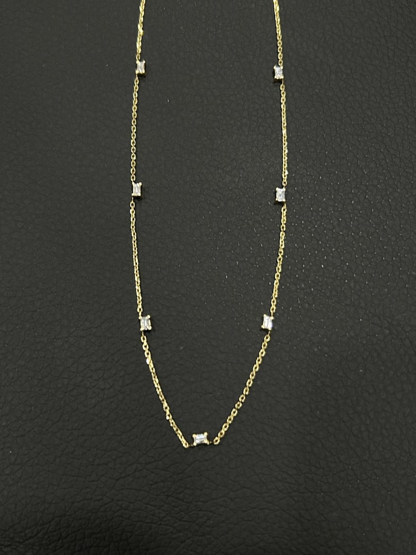 Gold necklace with small square diamonds evenly spaced along the chain on a dark background.