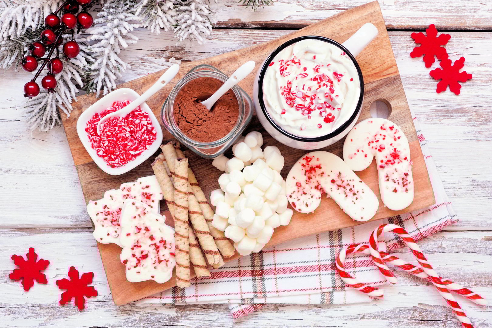 Christmas hot chocolate tray a variety of sweet toppings. Above view table scene on a white wood background.
