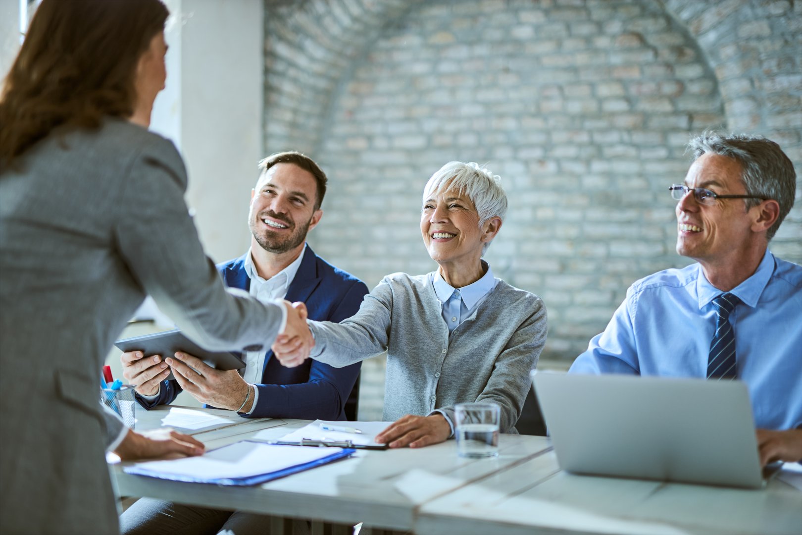 Happy member of human resource team shaking hands with female candidate on job interview in the office.