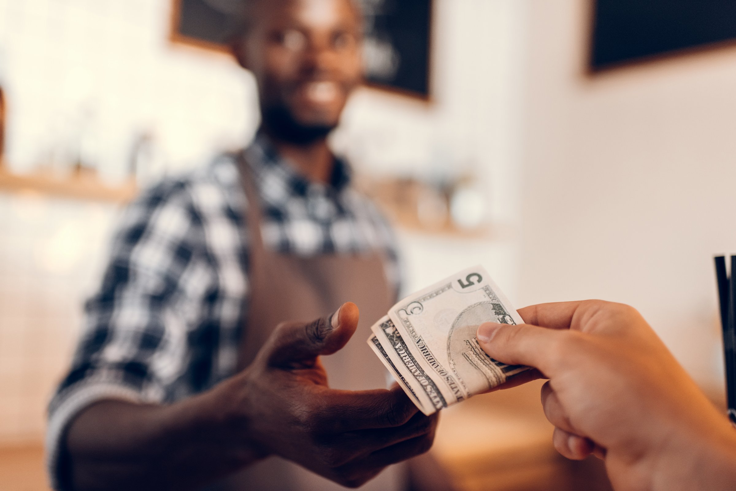 selective focus of african american barista taking cash payment on bar counter in cafe