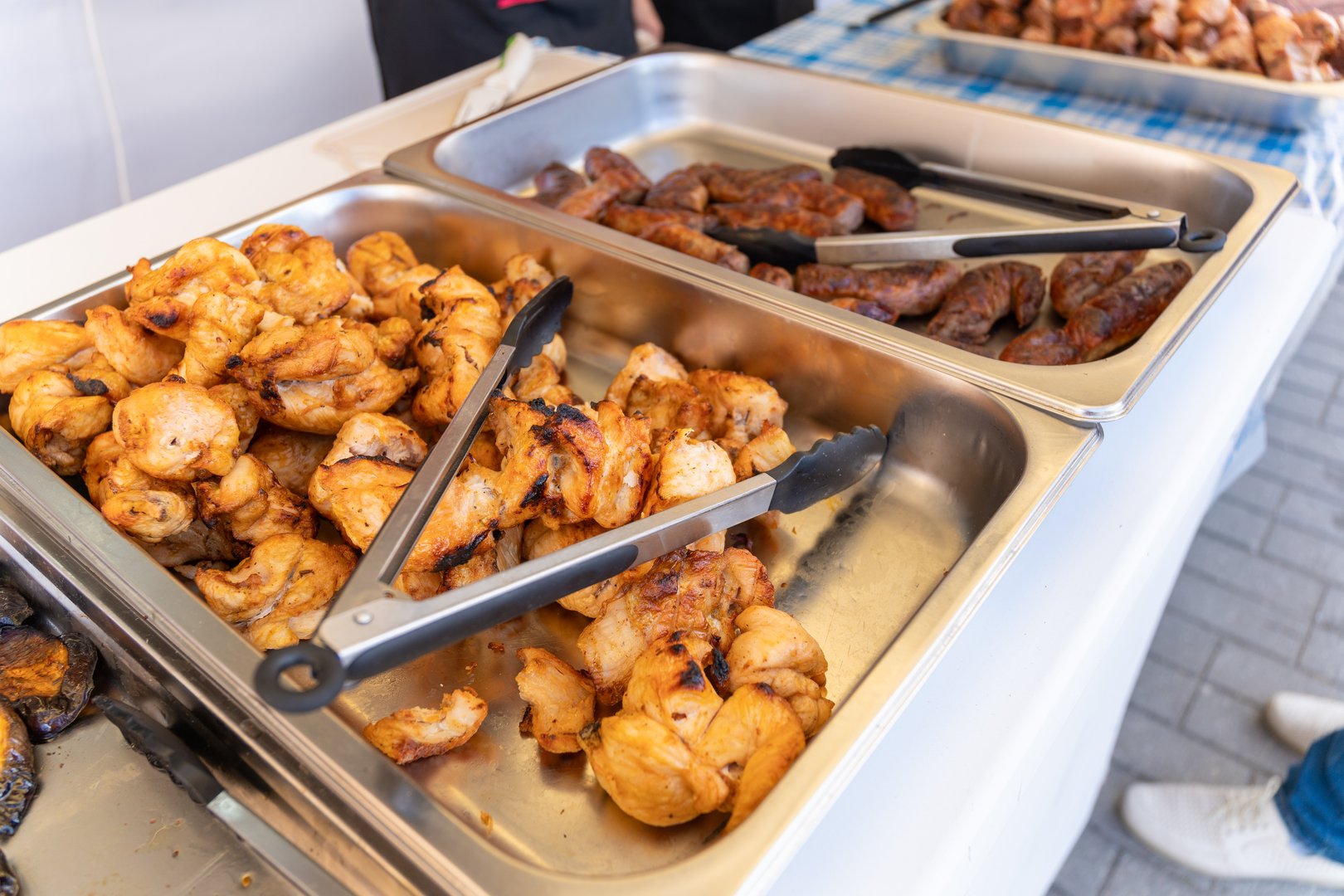 Grilled sausages and kebabs on serving trays at a Swedish table buffet. Self-service with provided tongs.