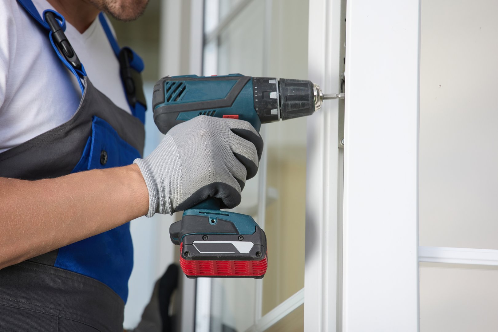 Experienced installer in uniform automatic screwdriver and repairs plastic door