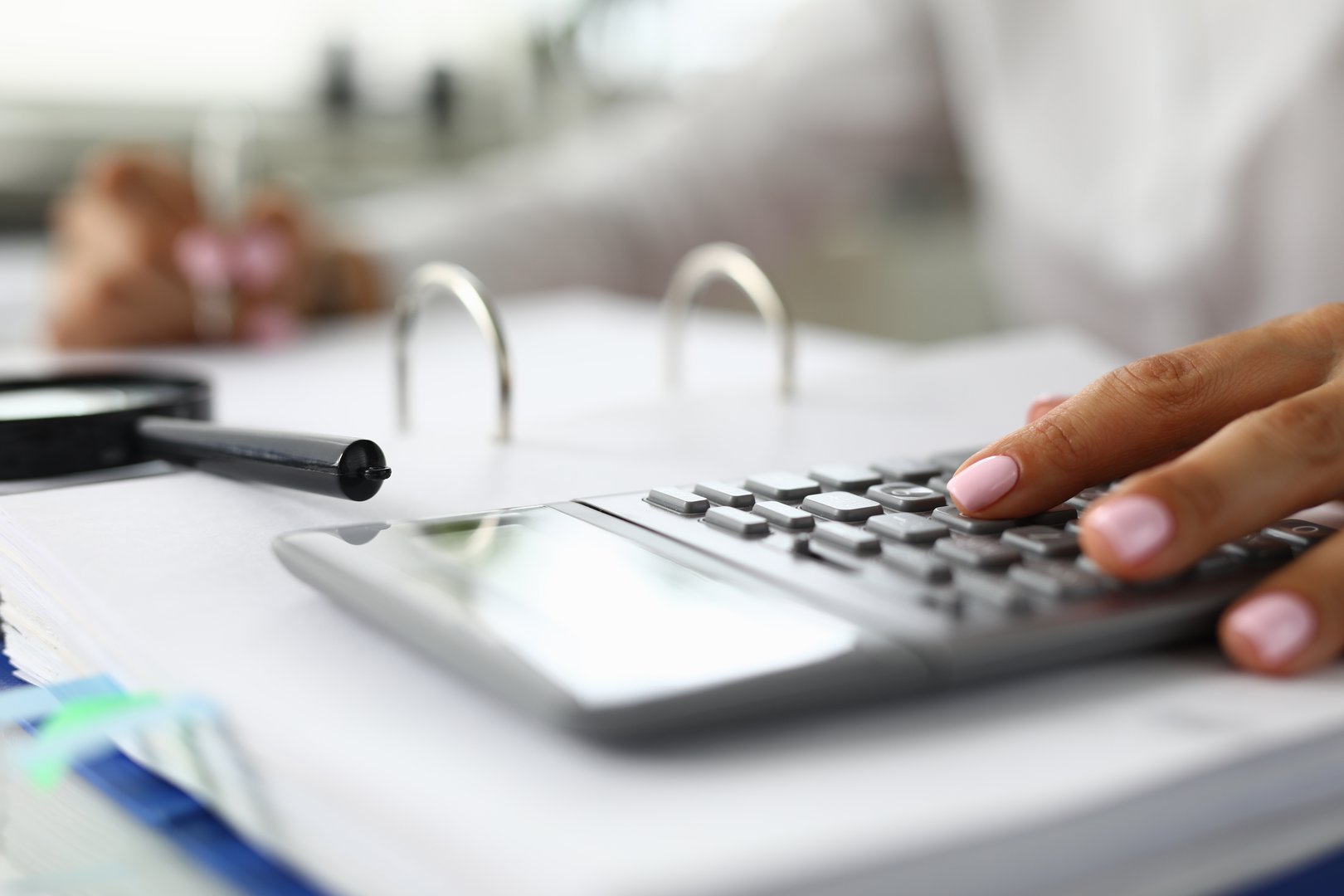 Women's hands on calculator next to magnifying glass and documents. Accounting and auditing services concept