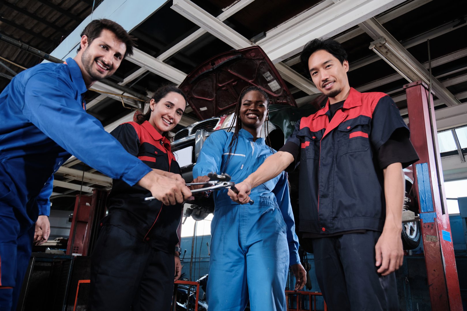 Harmonious professional mechanic teamwork, multiracial engineers with wrenches united, cheerful, and happy smile in fix car garage, maintenance service jobs in automotive transport industry station.