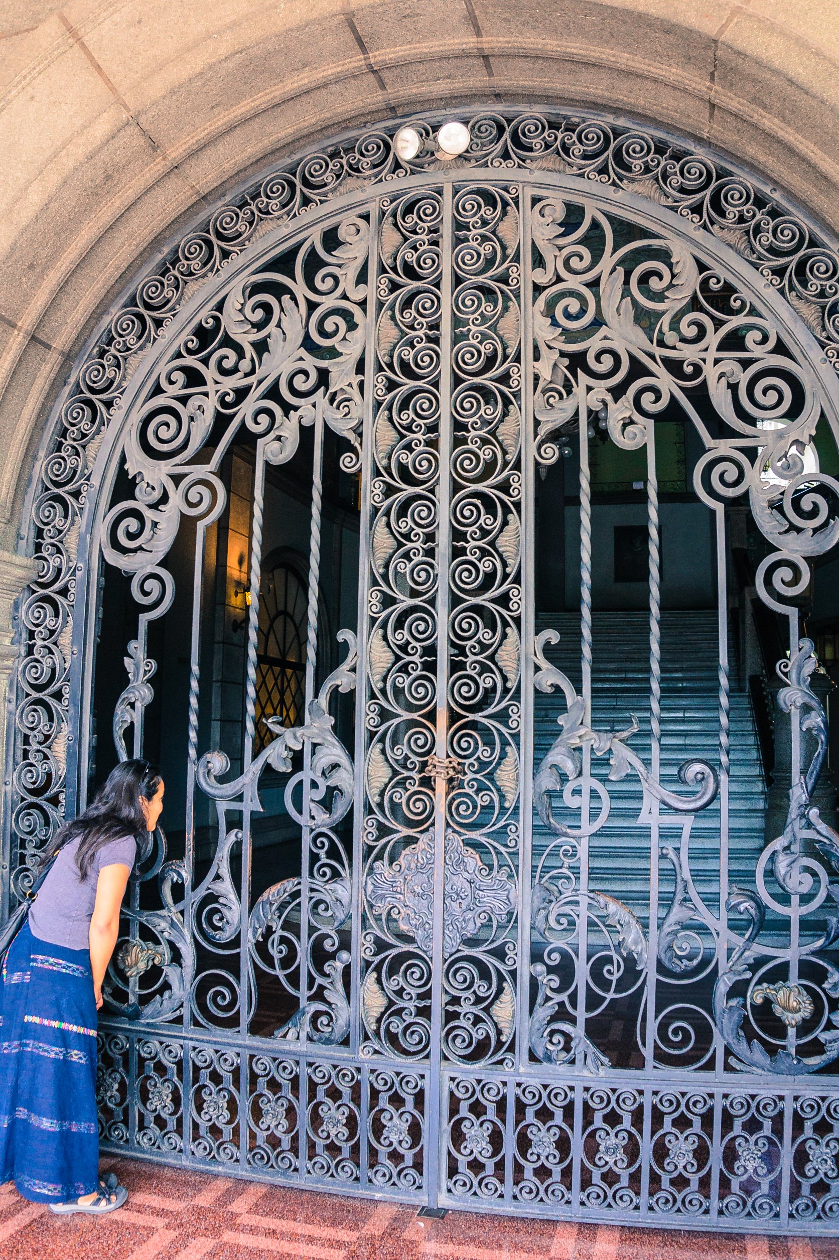 Hispanic woman looking through wrought iron gate into Palace