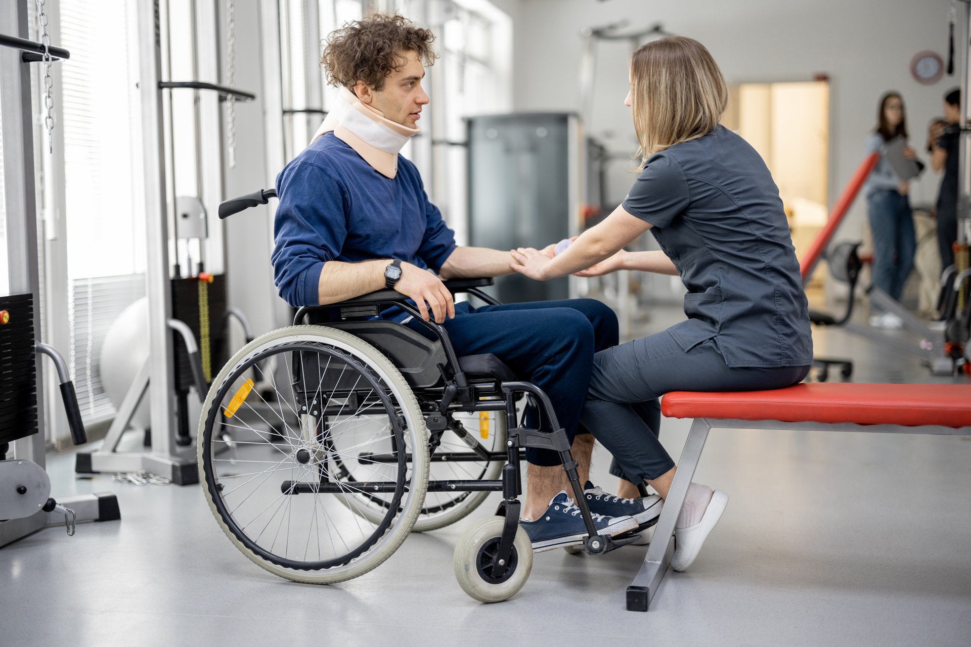 Rehabilitation specialist helps a guy to do exercises for recovery from injury, who is sitting in a wheelchair with a corset around his neck. Concept of physical therapy for people with disabilities
