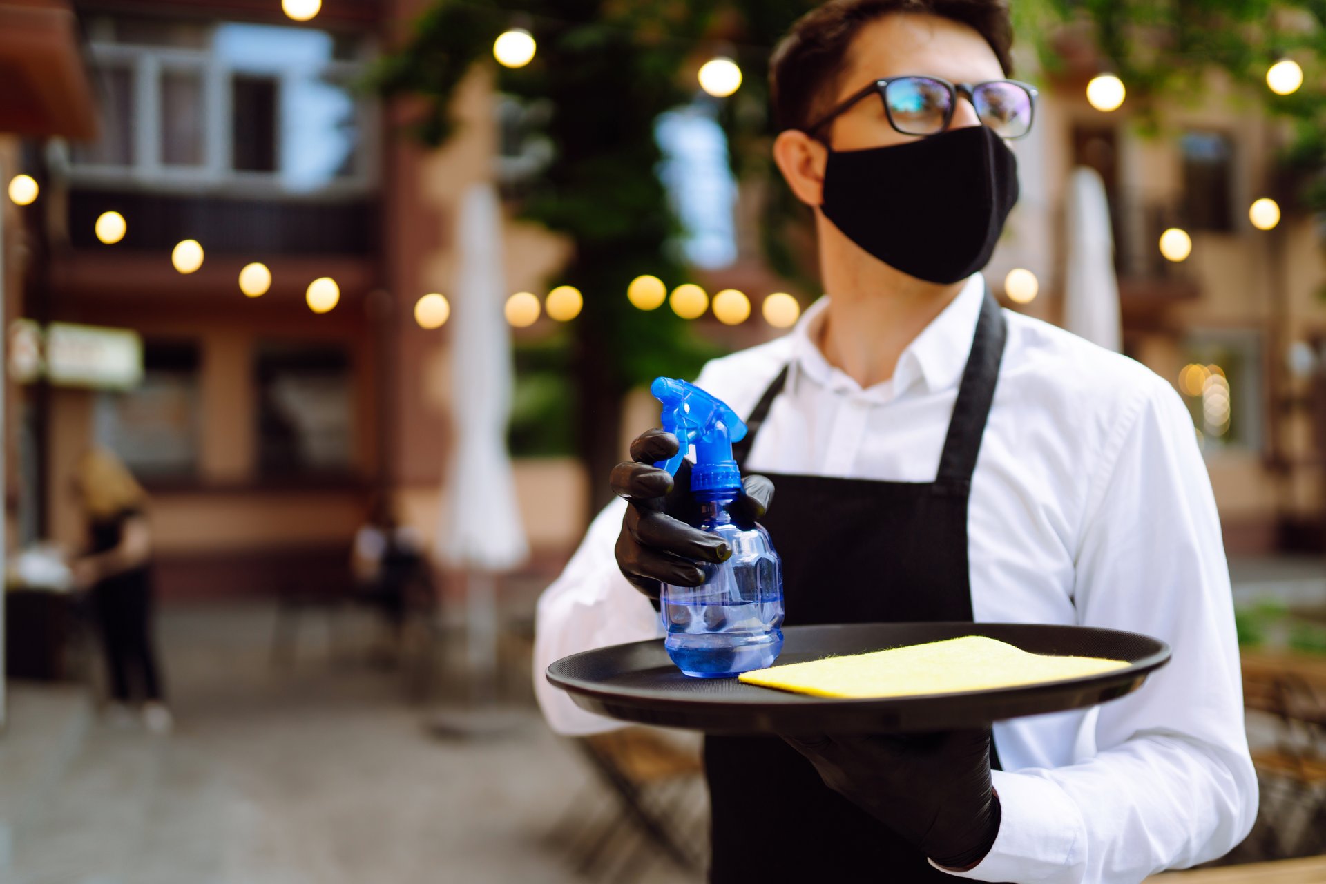 Mesero sirviendo bebida en restaurante al aire libre, con guantes de nitrilo negros.