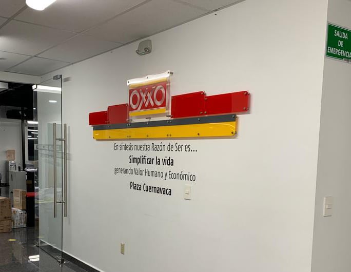 Wall with Oxxo logo and Spanish text about mission in Plaza Cuernavaca office hallway.
