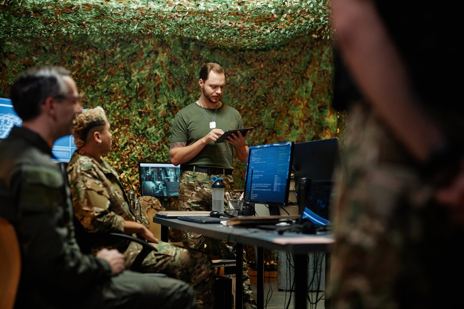 Young man using tablet while standing in front of colleagues in command and control center and making report about new surveillance system