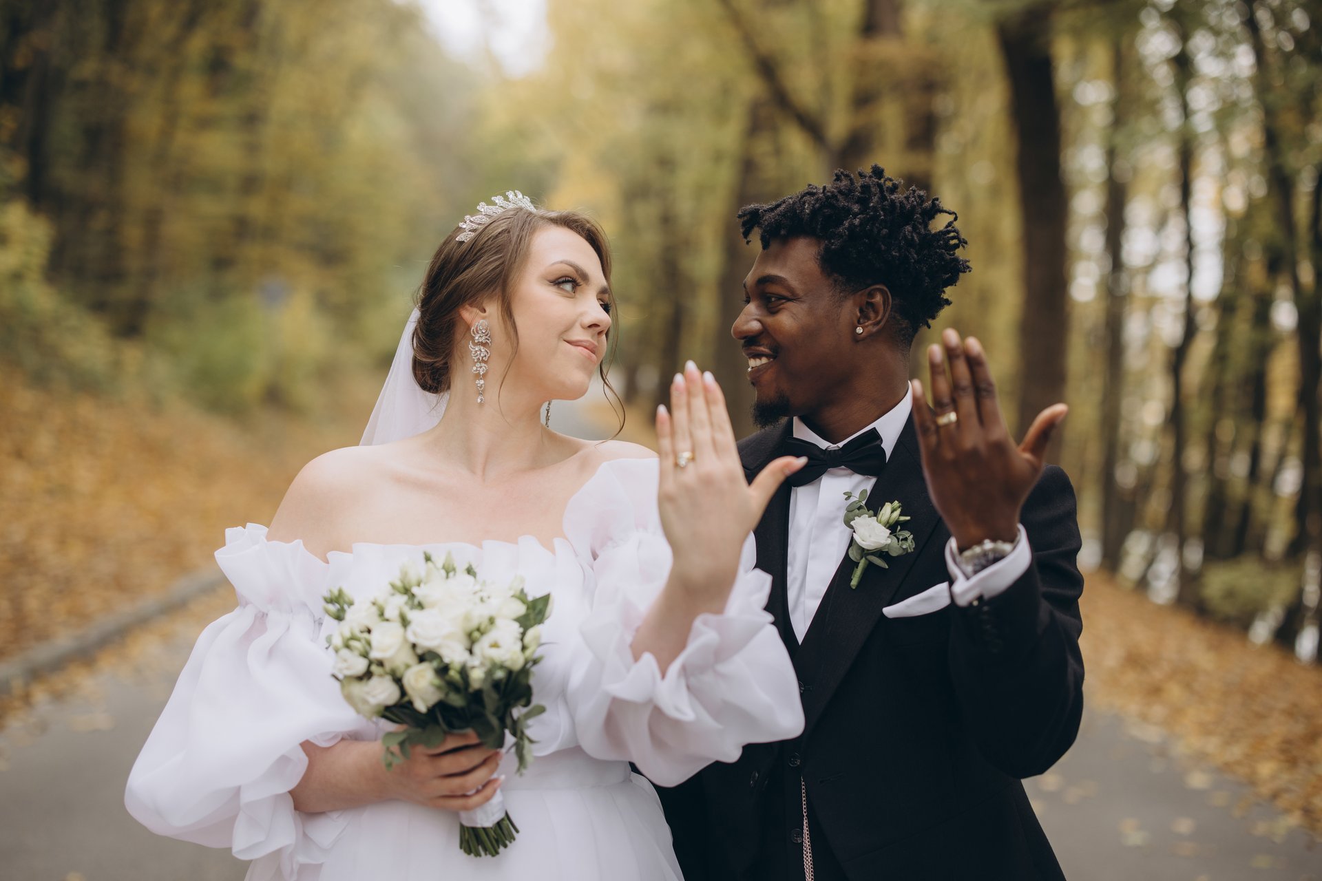 Newlyweds showing their wedding rings while enjoying a romantic moment in a beautiful autumn park