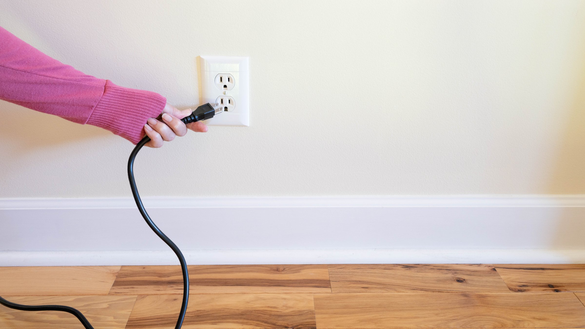 Hand placing or removing a power plug into or out of an American electrical wall outlet