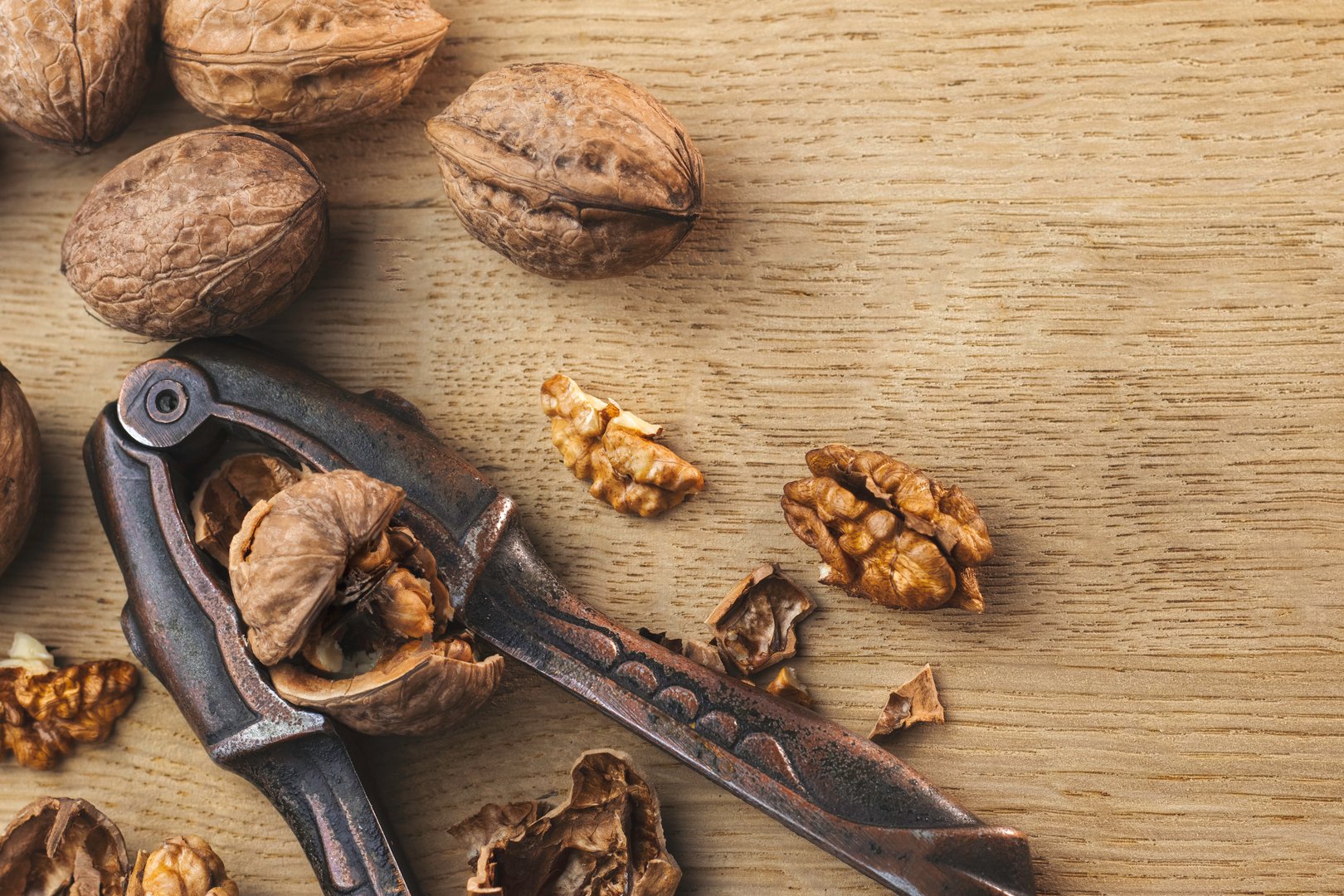 Metal old nutcracker cracks a nut, walnuts in shell, cracked, shell and kernels close-up lie on a wooden table surface. Super foods concept. Cracked nuts, apply force.