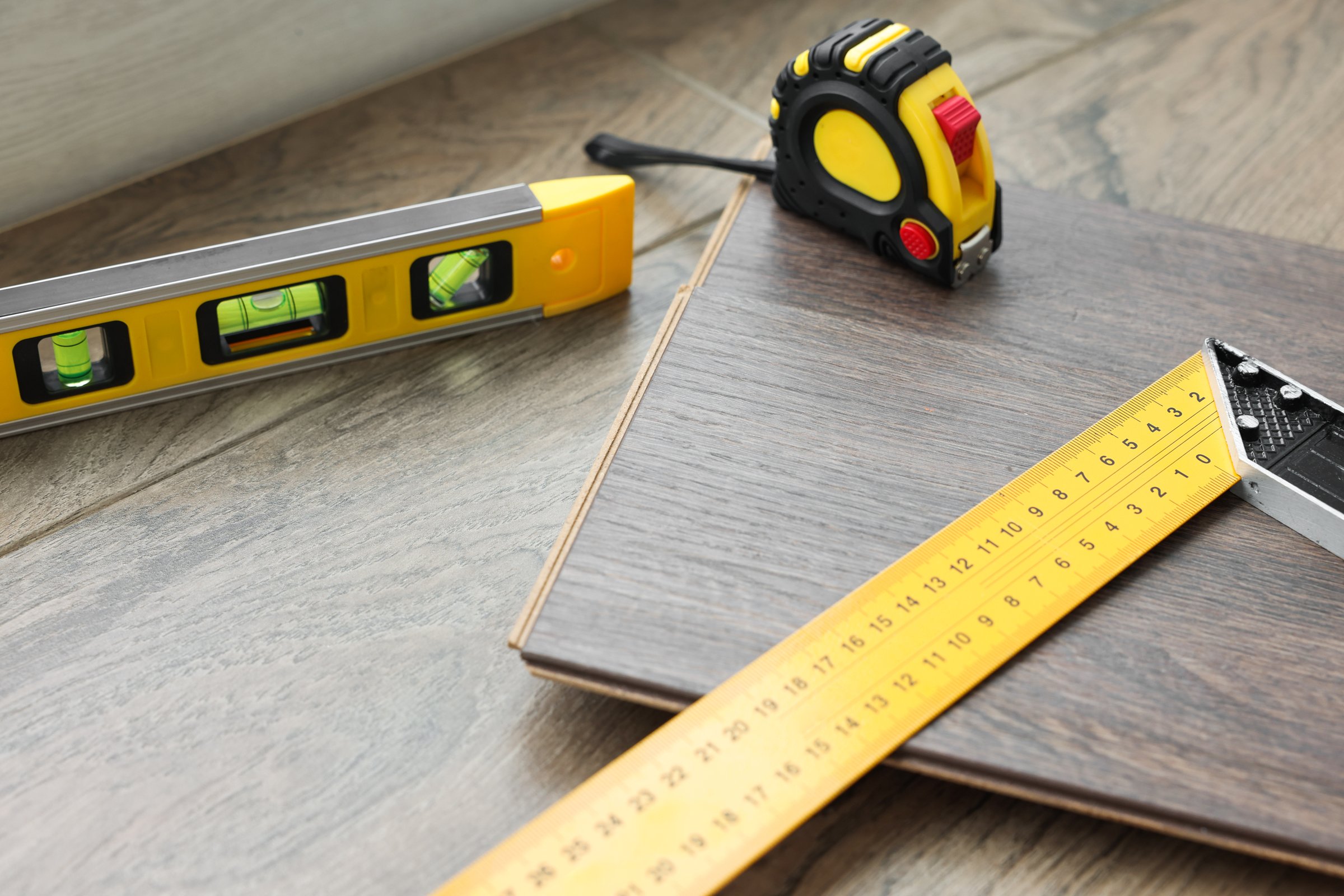 Measuring tools and laminate flooring pieces on wooden surface, closeup