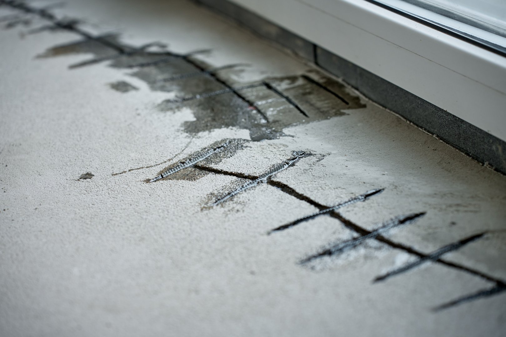 Repairing cracks in concrete floor near window using sealant. Renovation process in house under construction