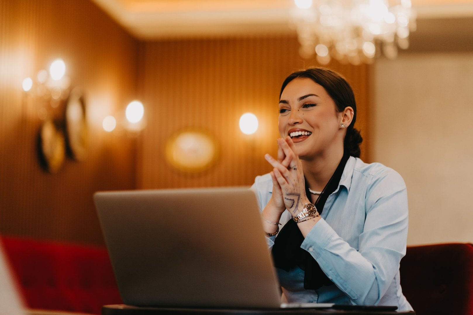 A charismatic Latina businesswoman confidently engages in a business meeting at a cafe, her laptop screen reflecting her presentation.
