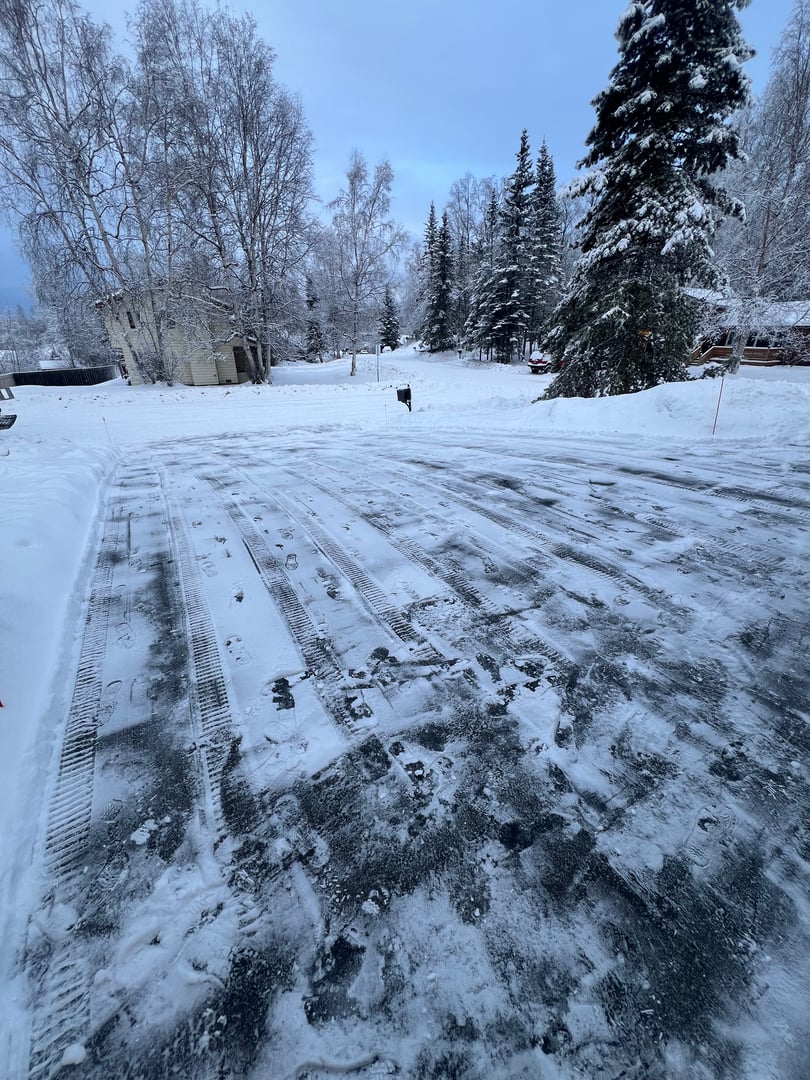 Snow-covered driveway after professional snow removal service in Anchorage, showcasing cleared path and tire tracks in fresh snow.