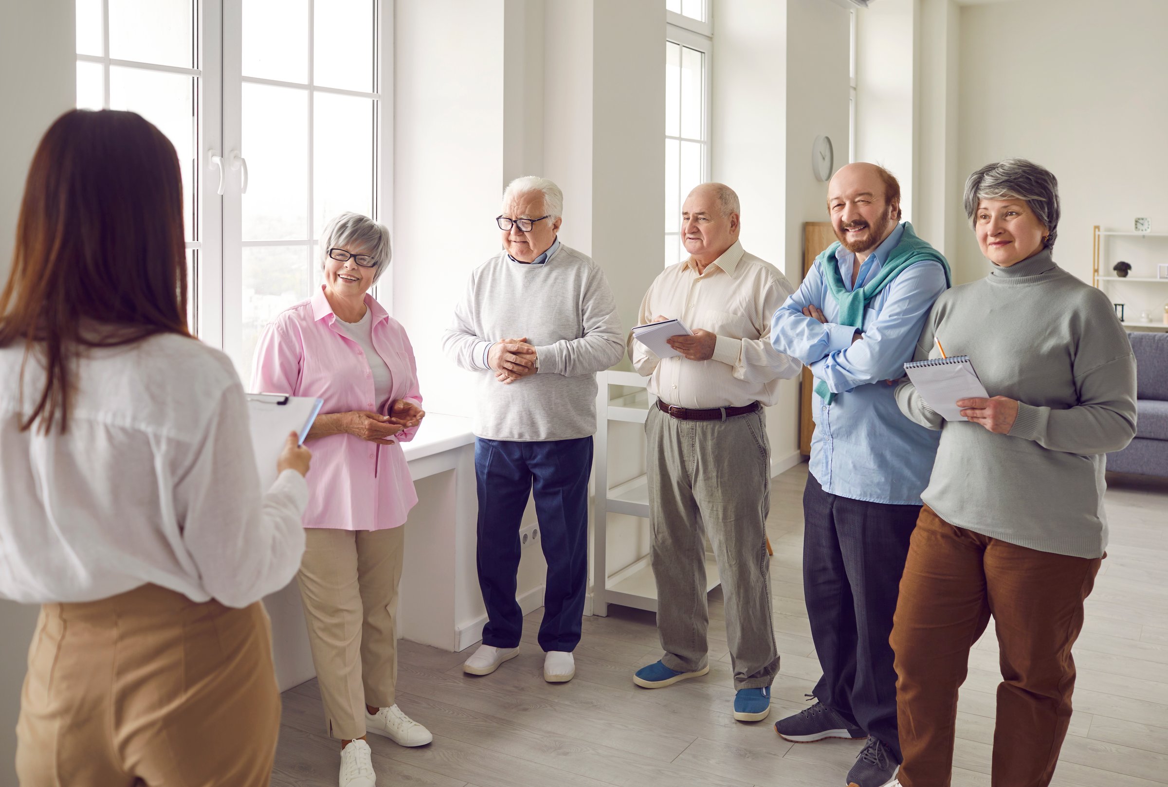 Group of mature people meeting with psychologist or business coach. Happy old, retired men and women listening to teacher and taking notes in notebooks. Senior education concept
