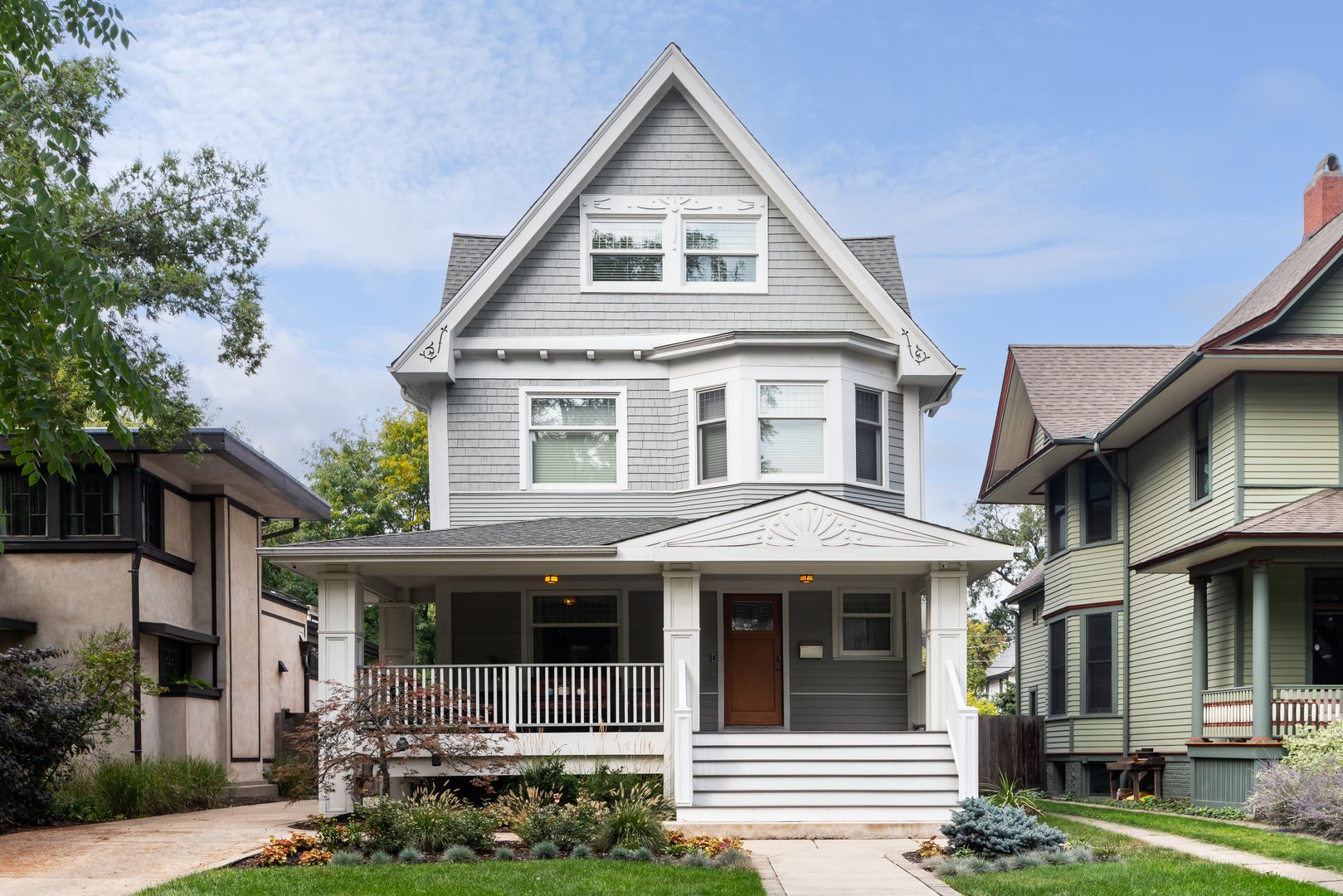 Chicago, IL, USA - September 20, 2023: A beautiful, grey and white cedar victorian home with a covered porch and well kept landscaping.