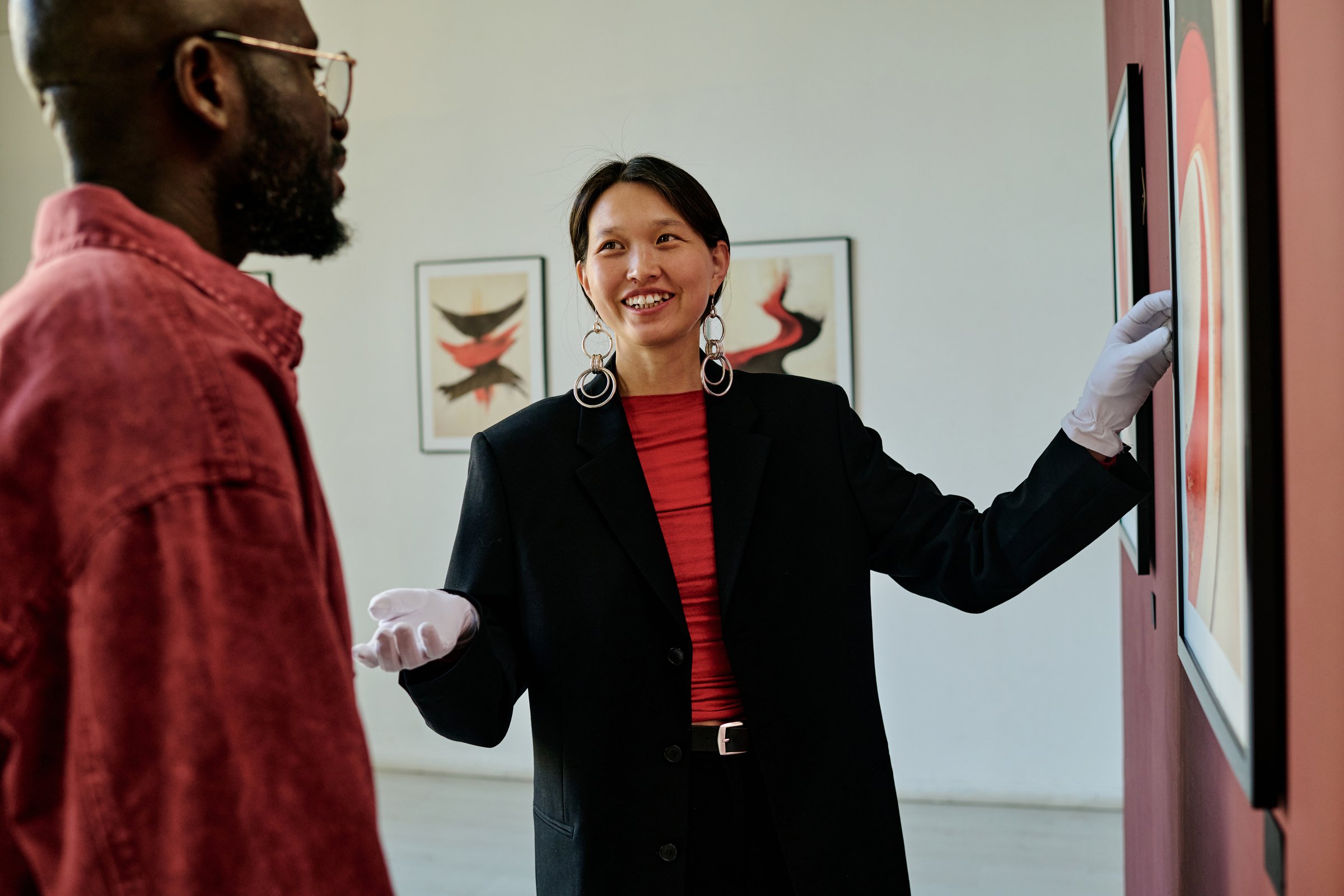 Art curator explaining contemporary art pieces to visitor while gesturing towards artwork on display. Artwork highlighted in clean gallery setting