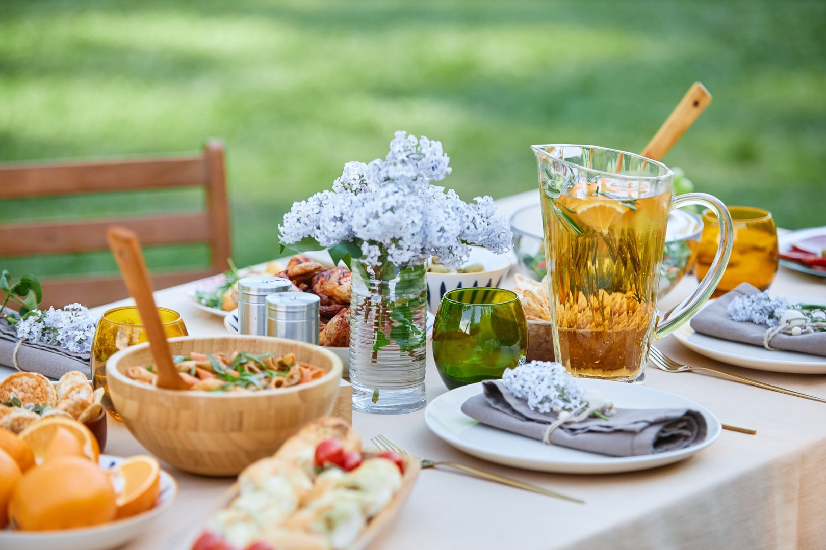 Elegant outdoor table set with fresh flowers, appetizers, and drinks on a wooden table perfect for gathering or event surrounded by greenery in the background