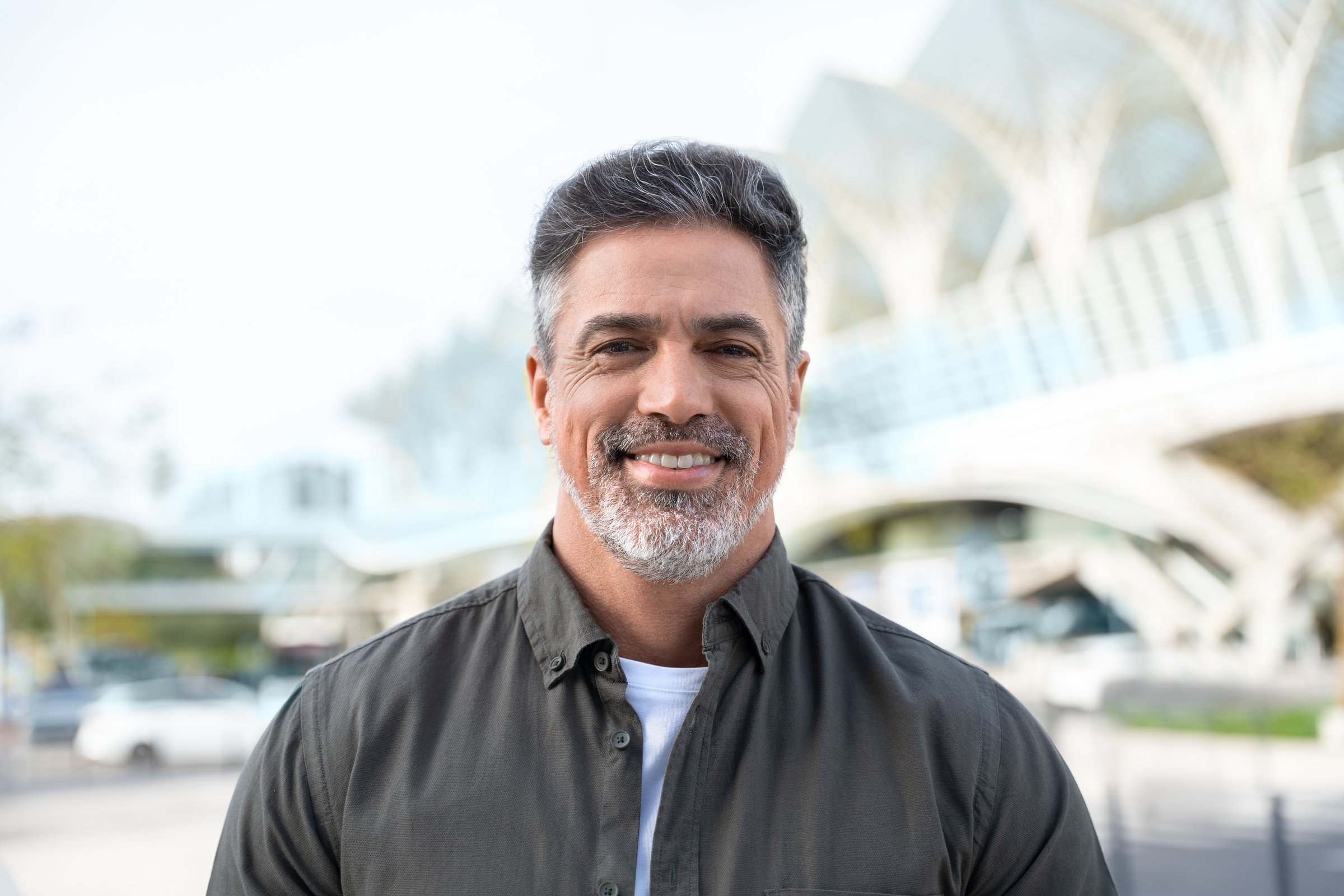 Lifestyle portrait of European middle age mature adult man. Freelancer entrepreneur standing outdoor at street. Happy handsome 40 years old latin hispanic businessman smiling at camera with sun ray