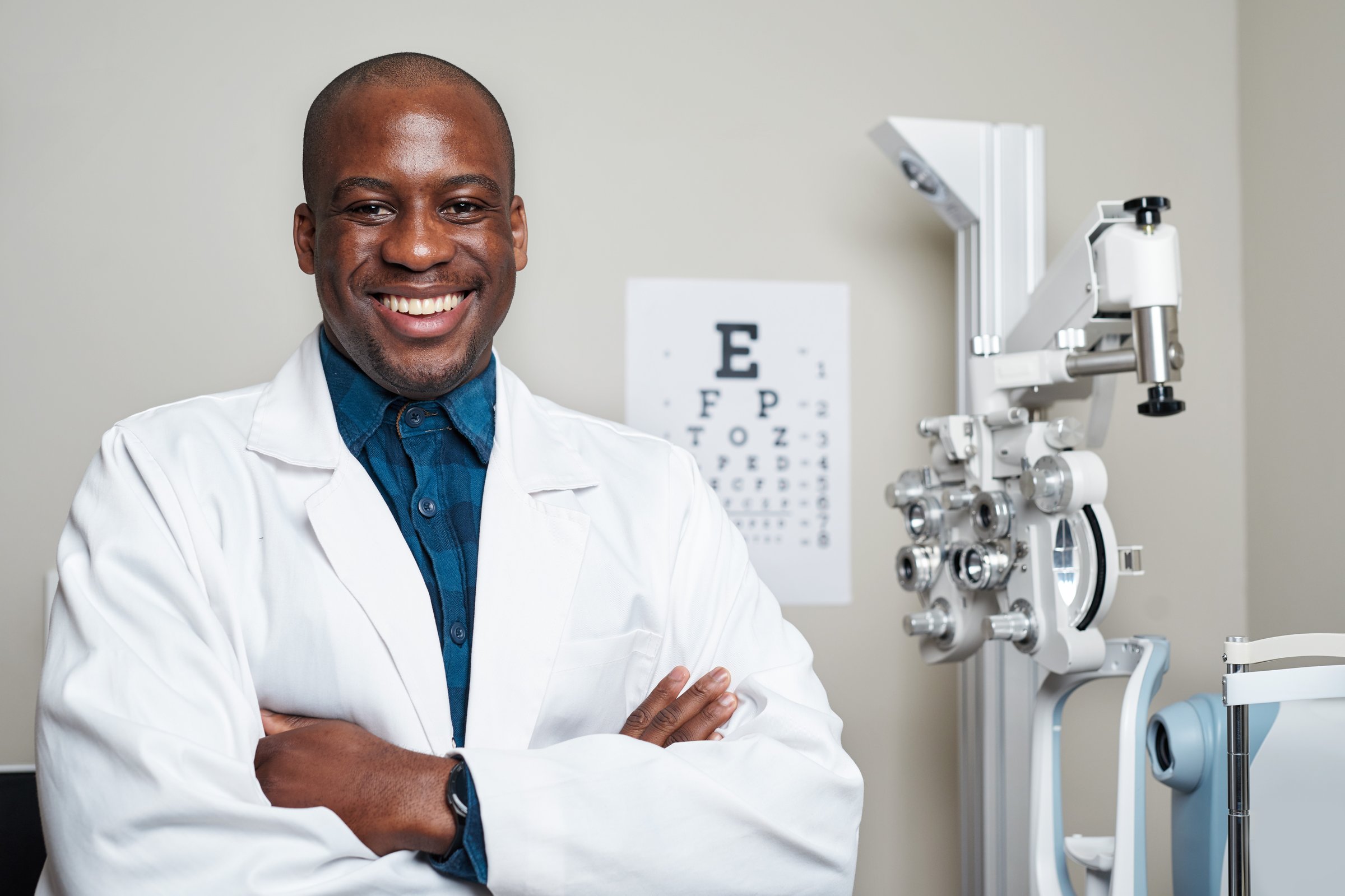 A professional optometrist stands confidently in a modern optometry office, wearing a white coat and smiling warmly. Surrounded by eye examination equipment, the business owner exudes a positive and welcoming atmosphere, focusing on eye care and precision.