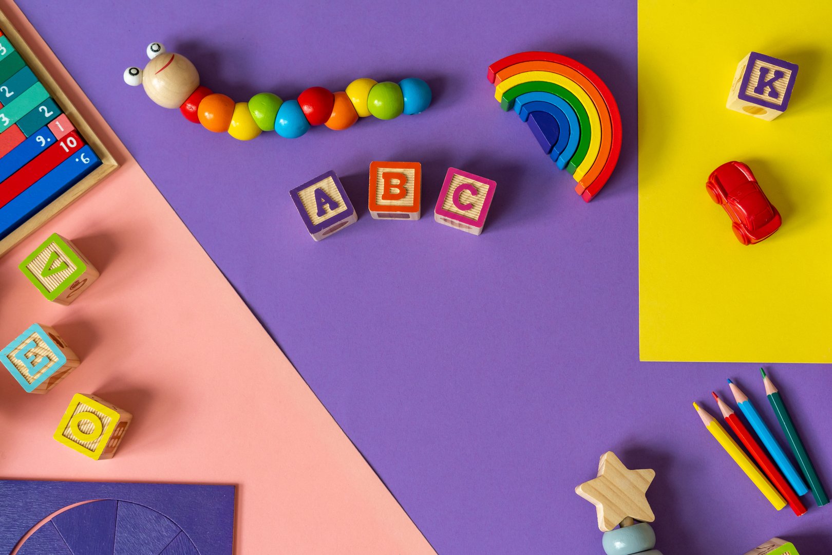 Wooden kids toys on colourful paper. Educational toys blocks, pyramid, pencils, numbers. Toys for kindergarten, preschool or daycare. Copy space for text. Top view