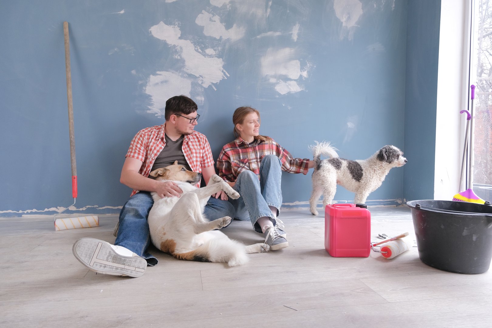 Happy couple renovating new house apartment , sitting on the floor with dogs . Home makeover, renovation concept
