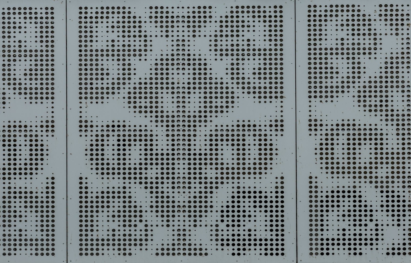 Close-up view of a gray metal surface featuring a decorative perforated design with evenly spaced circular holes. The geometric arrangement creates a symmetrical, abstract pattern that gives the material a modern and industrial aesthetic. The texture highlights precision, repetition, and minimalism in design.