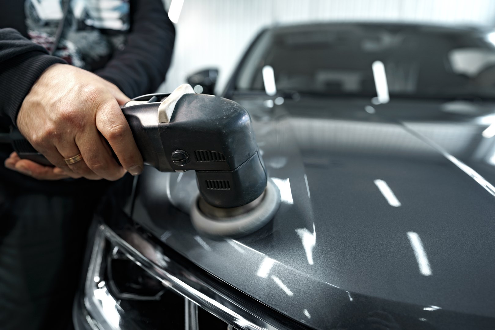 Car detailing. Male hands with orbital polisher in auto repair shop, close up